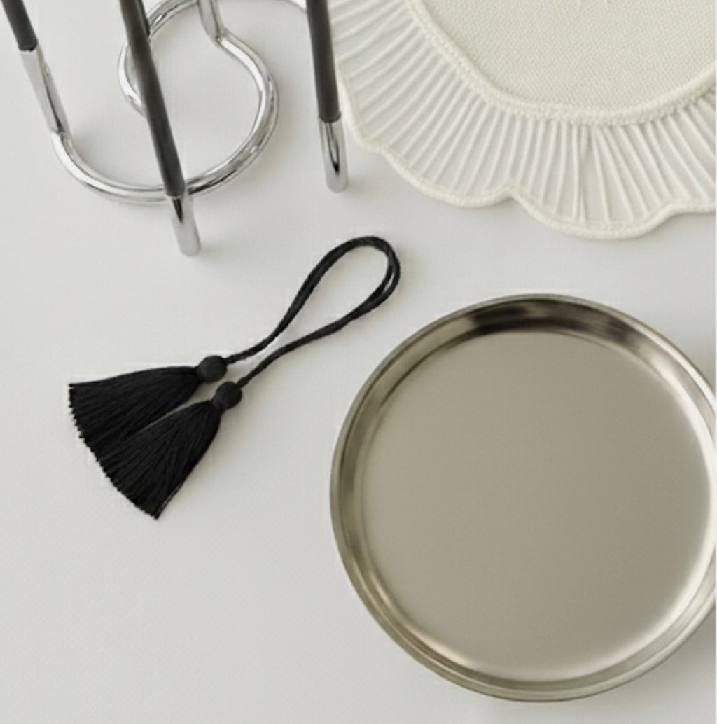 Round metallic tray with black tassel on a light surface